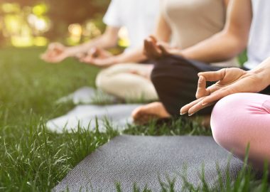 Yoga background. Group of people meditating outdoors, sitting in lotus pose in park, copy space